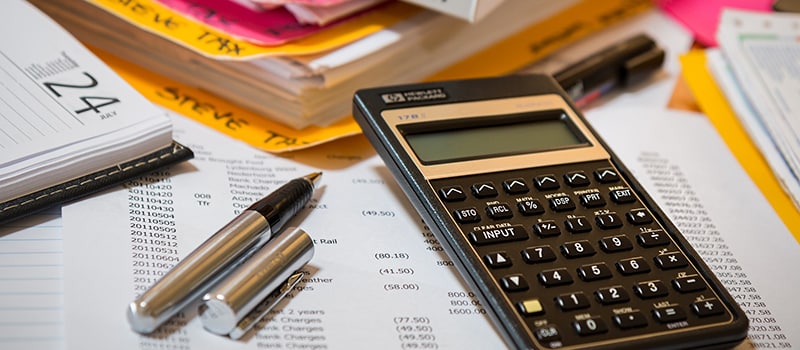 Pöydällä verotusta koskevia asiakirjoja, kalenteri, laskin ja kynä.